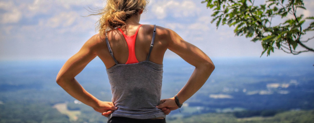 Frau stet auf Hügel und überblickt Landschaft. optimumtraining.at