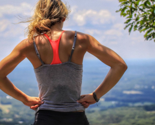 Frau stet auf Hügel und überblickt Landschaft. optimumtraining.at